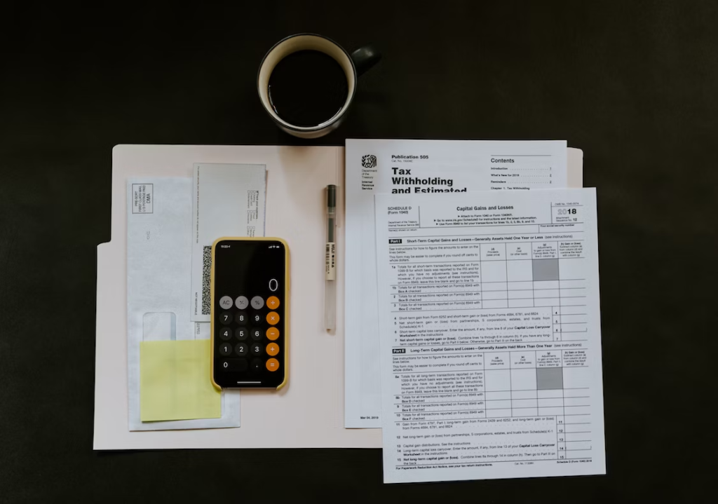 A flatlay image of tax documents, calculator, and pen, and other documents on a black table.