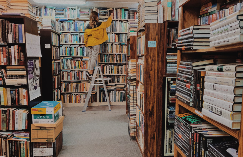 A woman on a ladder in a new bookstore, arranging books.
