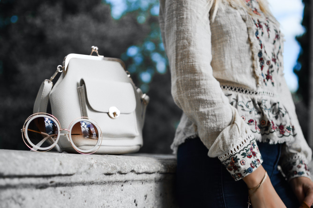 A girl in white blouse with white sunglasses and handbag beside her.