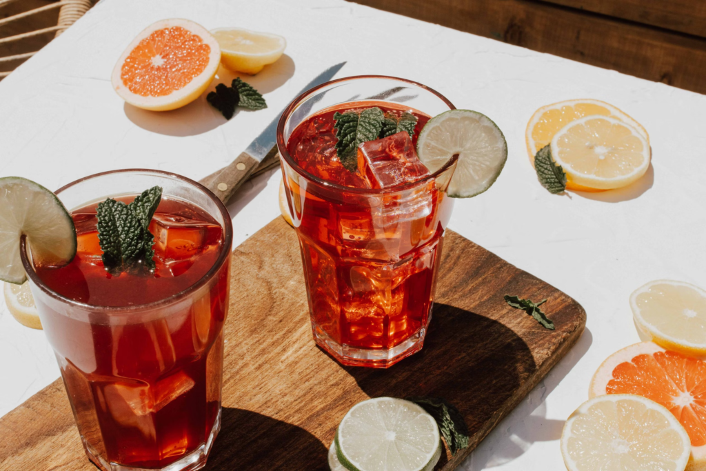 Two clear drinking glasses filled with red  beverage and decorated with mint leaves and lime slices on the glass rim.