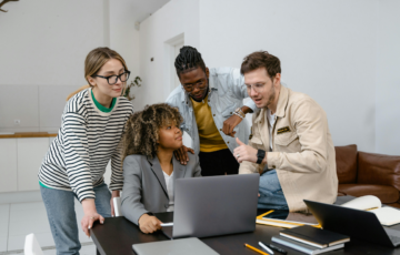 A team gathered around a laptop discussing viral trends and social media marketing strategies.