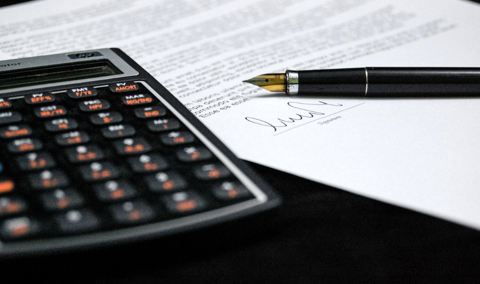 A calculator next to a piece of paper and a pen.