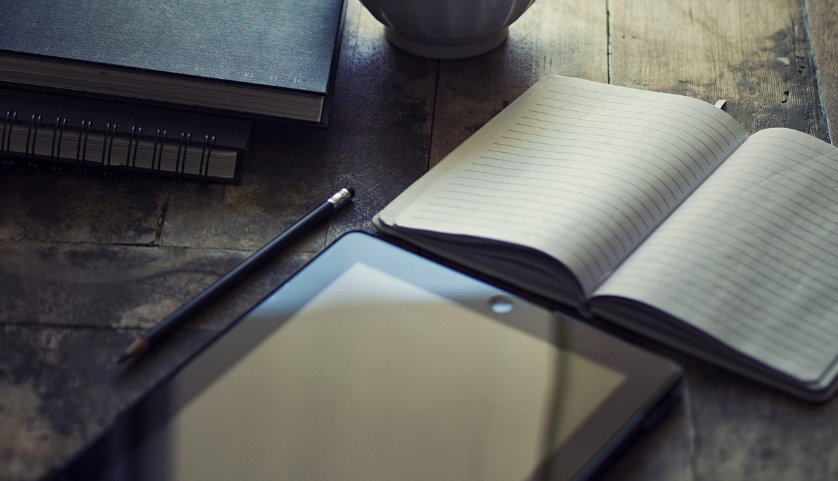 An open notebook next to a tablet and a pen.