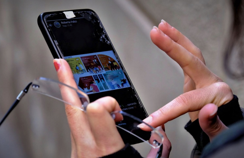 A person scrolling through a phone while holding a pair of glasses.