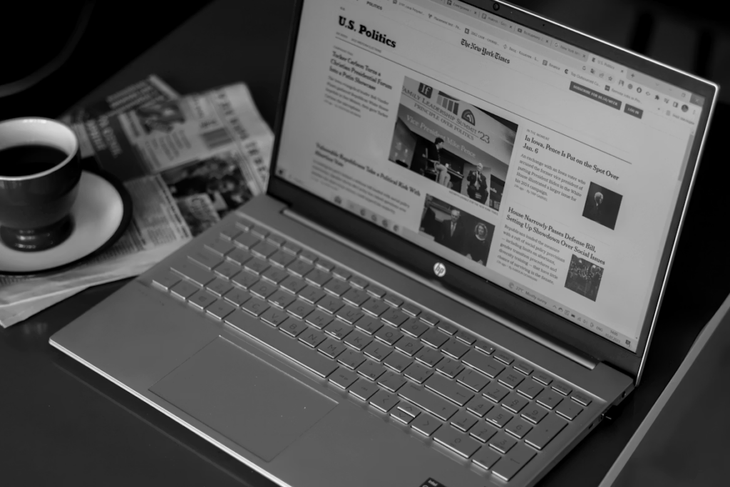 A laptop displaying a news website next to a newspaper and a cup of coffee.
