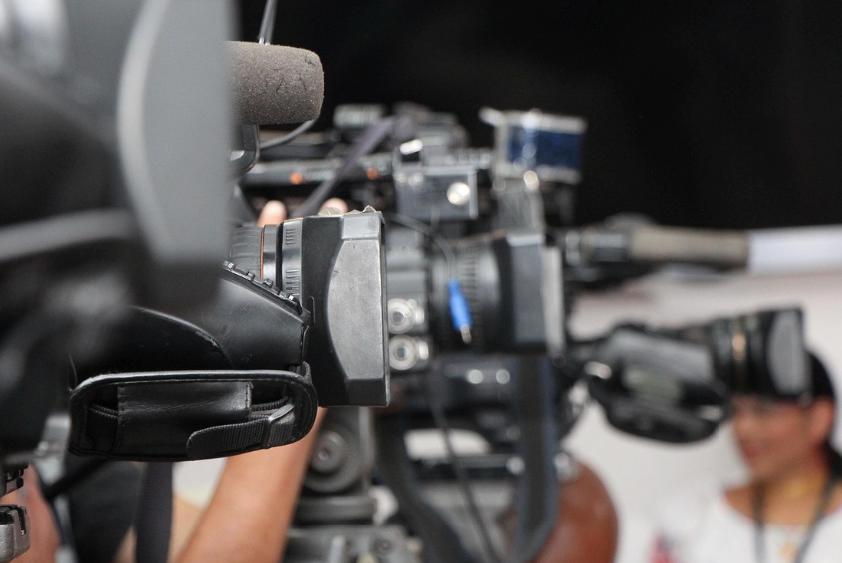 Journalists filming a brand press conference, showing the media-facing nature of press releases.
