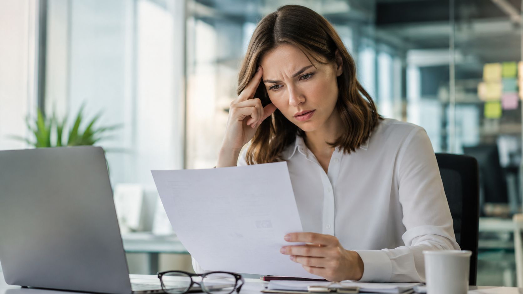 A concerned professional woman analyzing documents while working at her desk in a modern office environment.